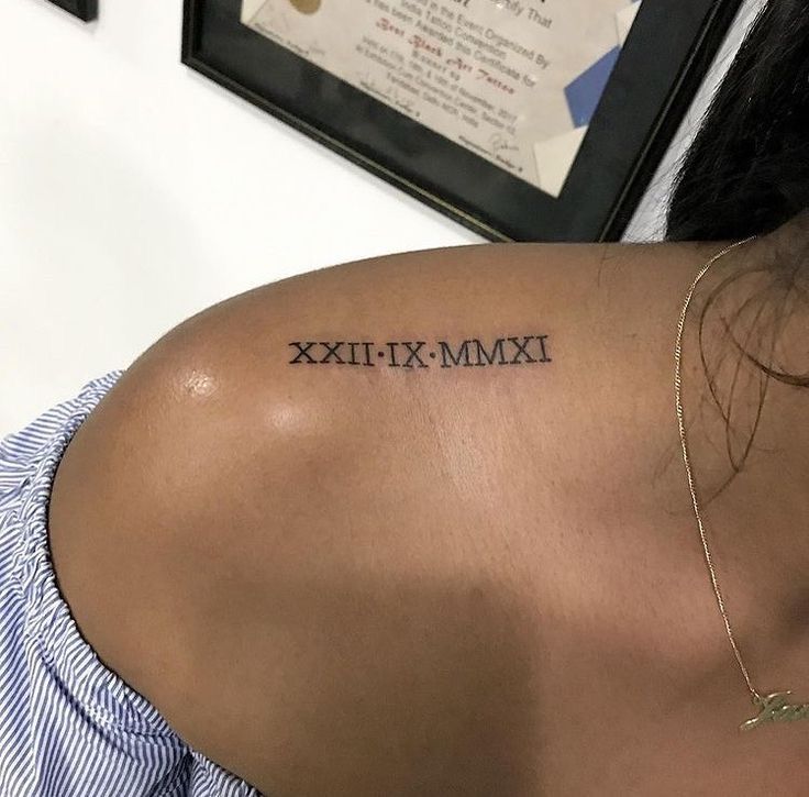 the back of a woman's shoulder with roman numerals tattooed on it