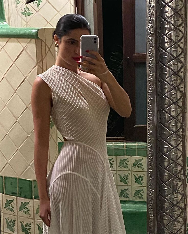 a woman in a white dress taking a selfie with her cell phone while standing in front of a mirror