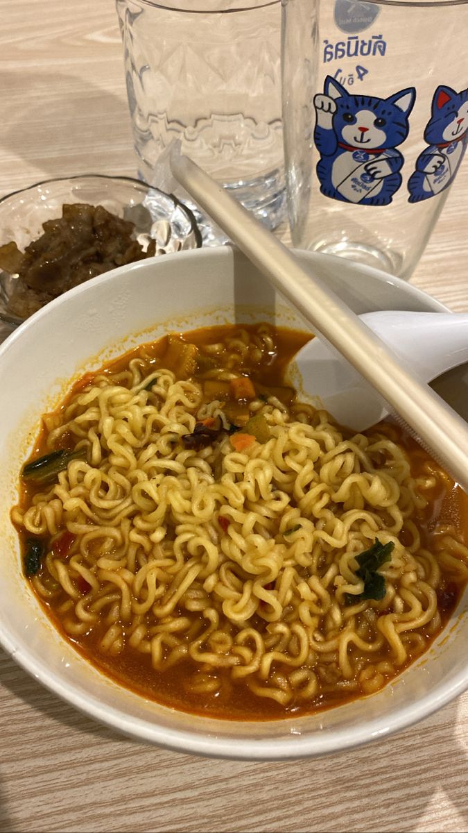 a bowl of ramen with chopsticks on a table next to two glasses