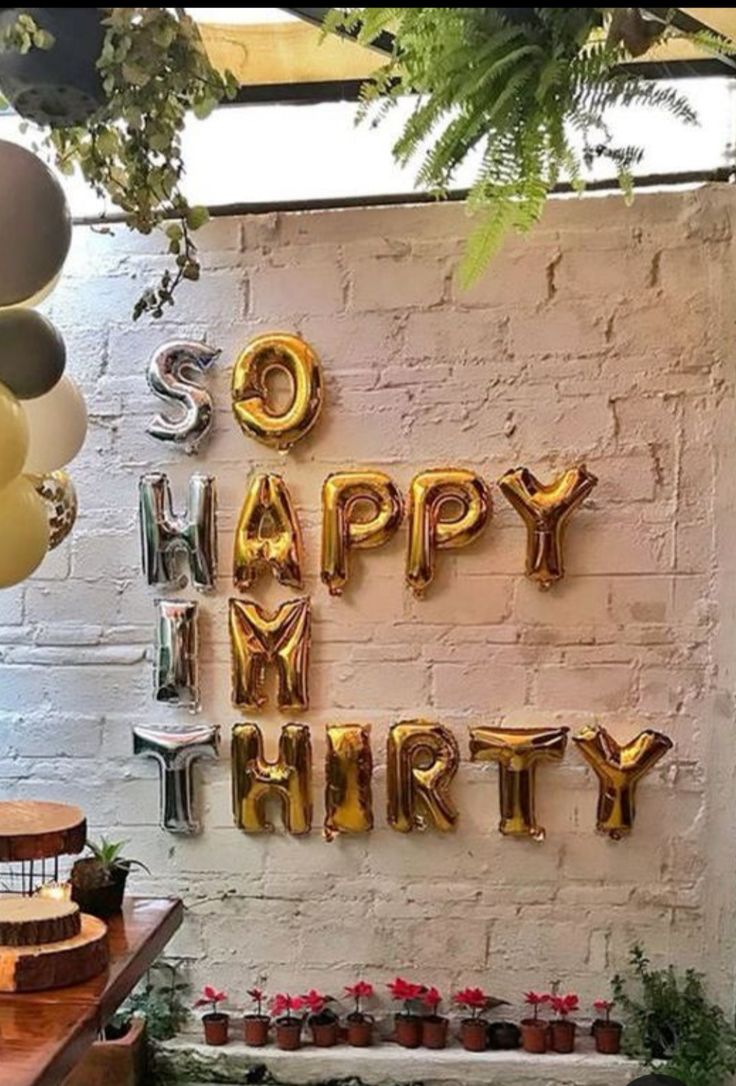 a birthday party with balloons, cake and decorations on the table in front of a brick wall