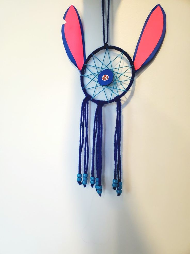 a wall hanging made to look like a bunny ears dream catcher with blue beads and pink ears