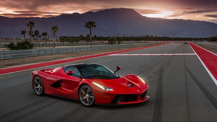 a red sports car driving on a race track with mountains in the background at sunset