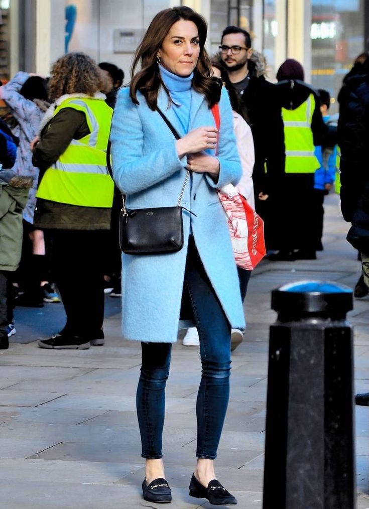 a woman is walking down the street with her hand in her pocket and wearing a blue coat