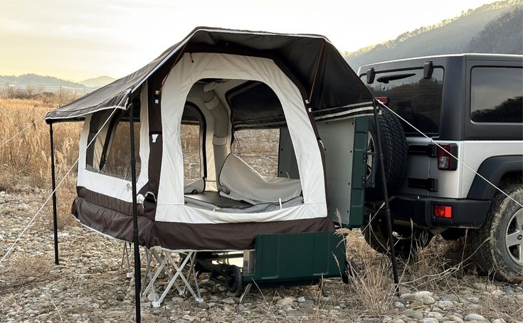 an suv parked next to a tent in the middle of a field with mountains in the background