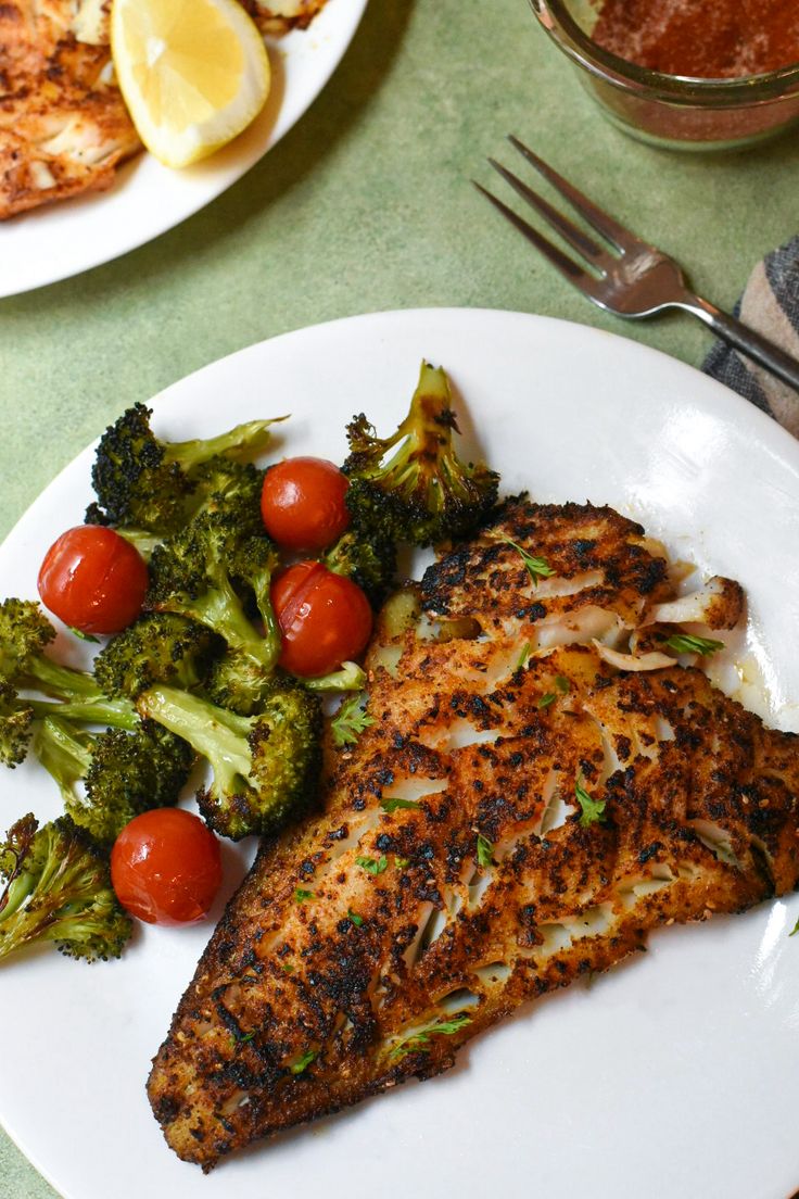 a white plate topped with fish next to broccoli and cherry tomatoes on top of a table