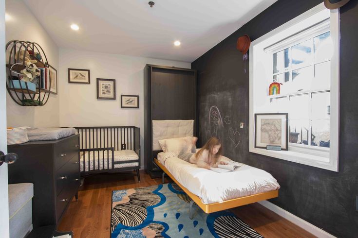 a child is laying on a bed in a room with black walls and wooden floors