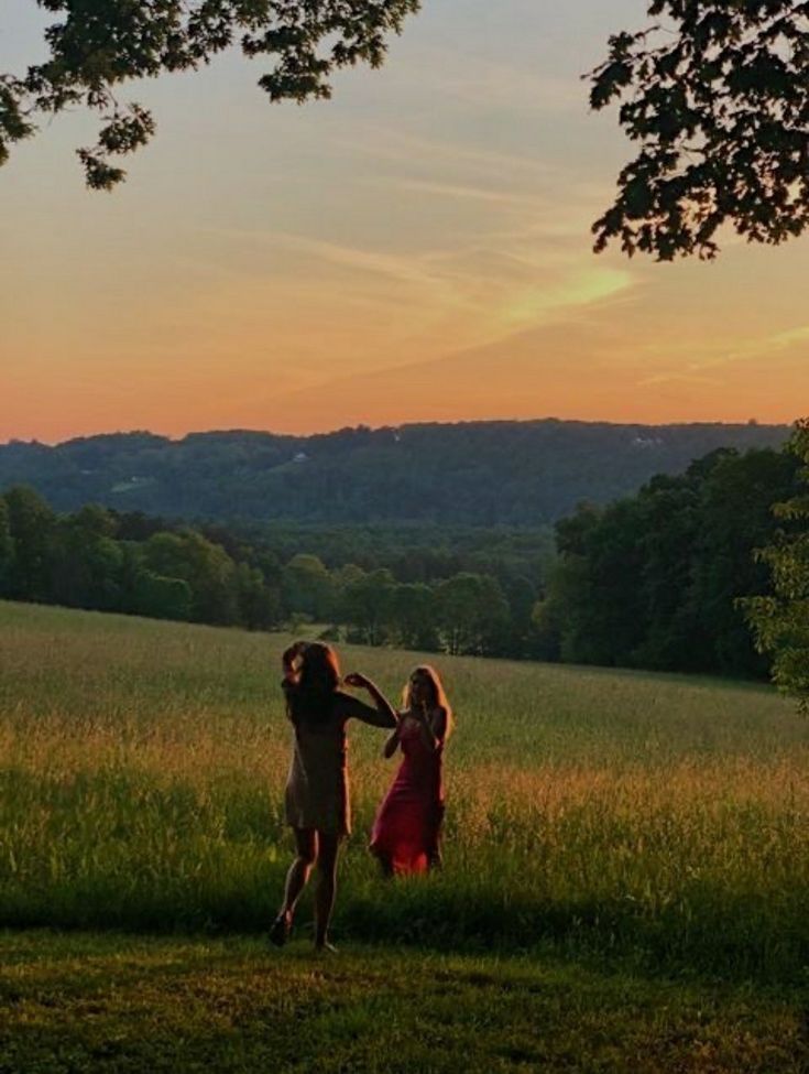 two girls are standing in the grass with their arms around each other as the sun sets