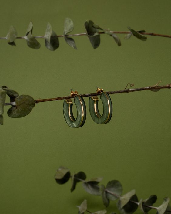 two pairs of earrings hanging from a twig on a green background with eucalyptus leaves