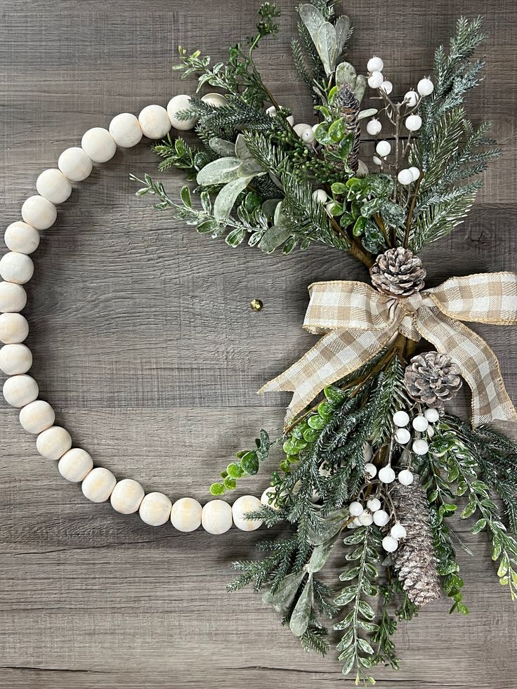 a christmas wreath with pine cones and greenery on a wooden background, decorated with white balls