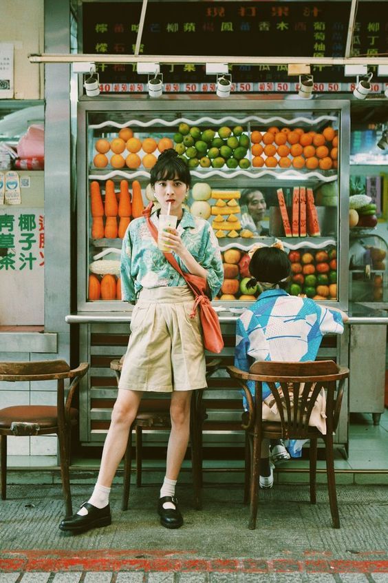 a man sitting at a table in front of a fruit stand while holding a cell phone to his ear