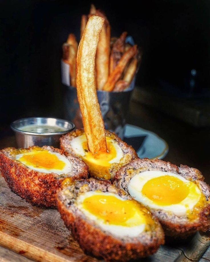 some fried eggs are on a cutting board next to french fries and dipping sauces