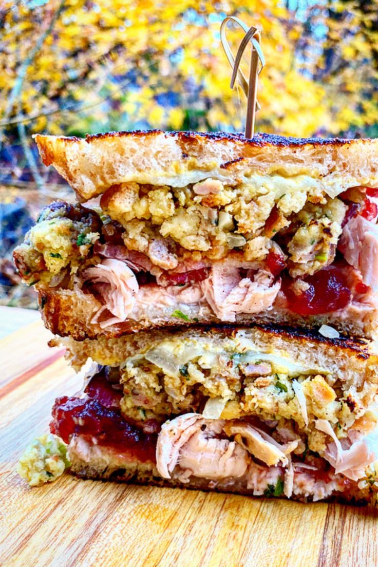 two sandwiches stacked on top of each other with meat and vegetables in between them, sitting on a wooden surface