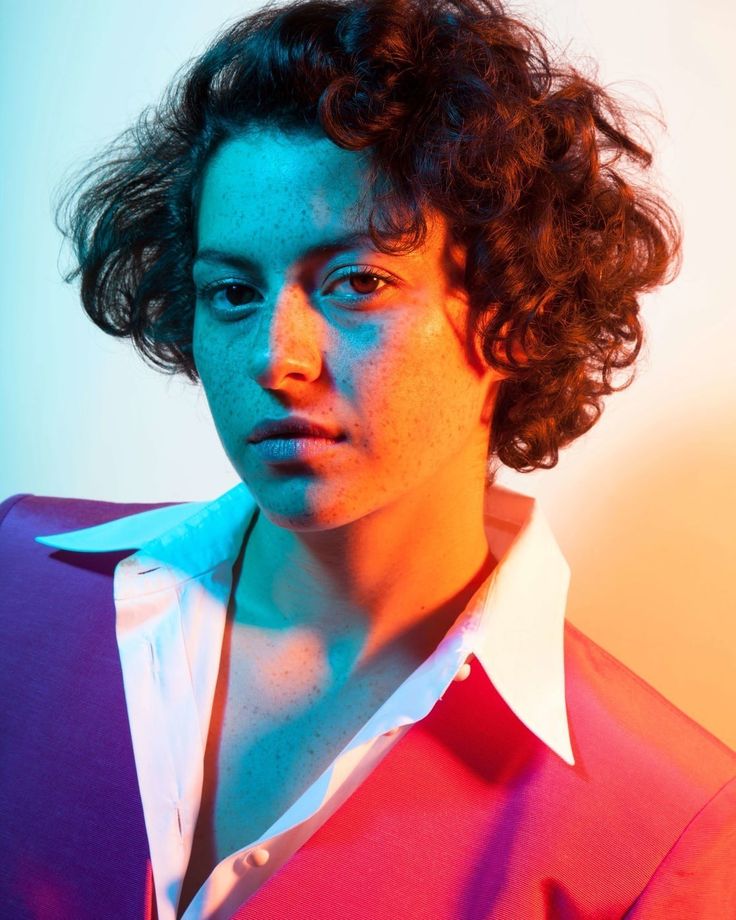 a woman with curly hair wearing a red shirt and white collared shirt looking at the camera