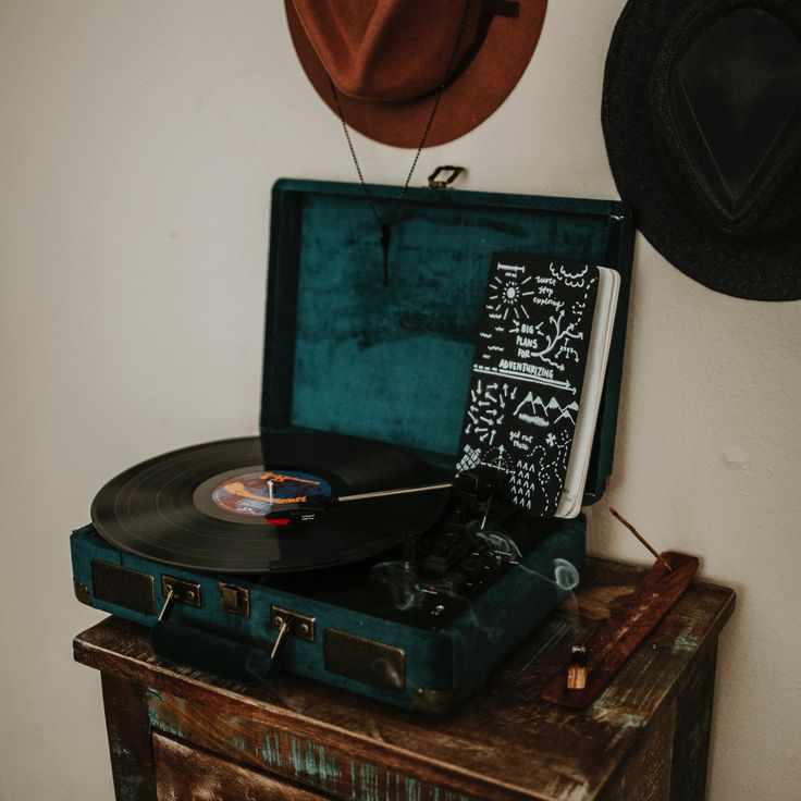 an old record player sitting on top of a piece of luggage next to a hat