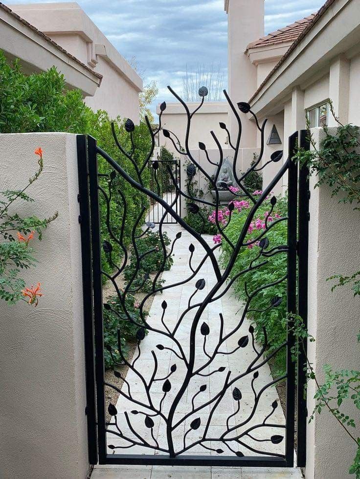 an iron gate in the shape of a tree with leaves and flowers on it, leading into a courtyard