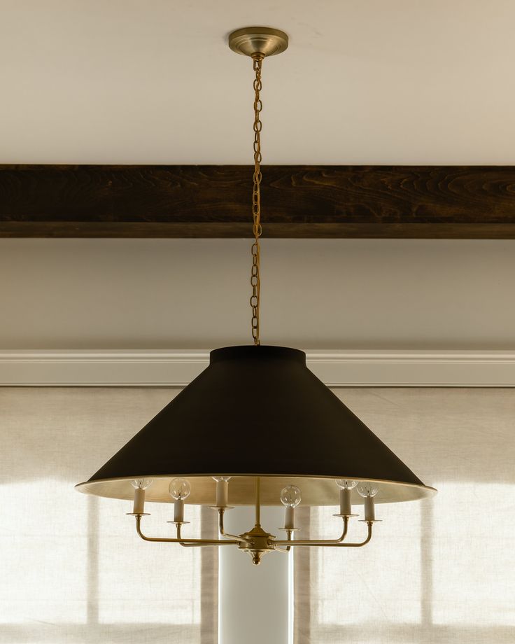 a black lamp hanging from the ceiling in a room with white walls and wooden beams