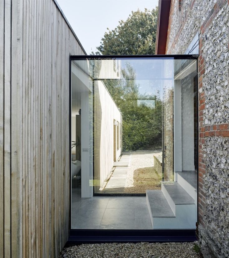 an open glass door on the side of a building next to a brick wall and trees