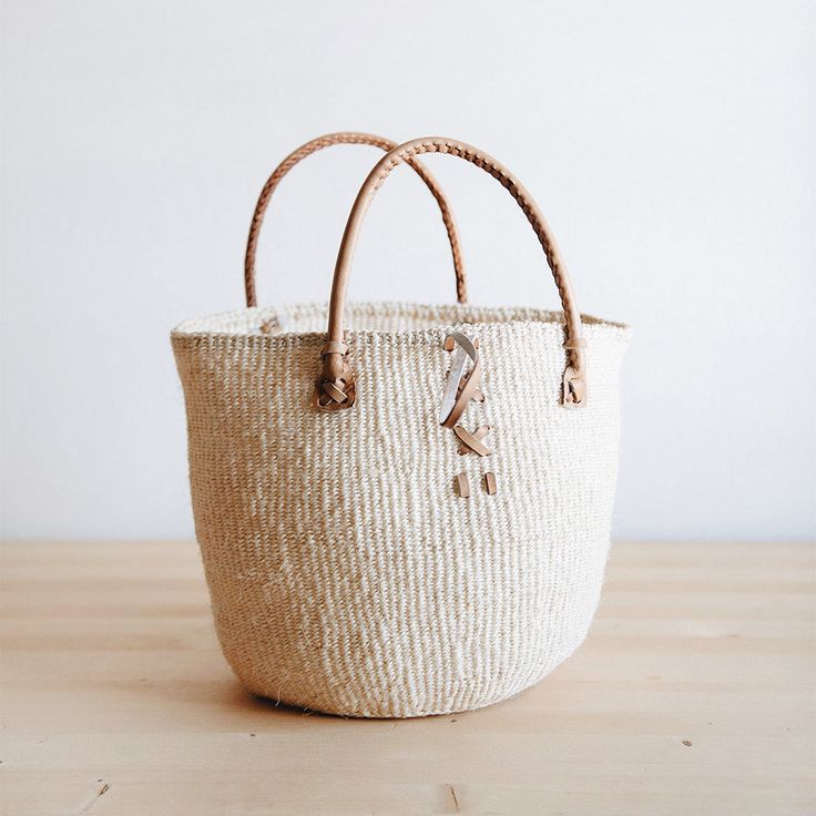 Rural Kamba women in Kenya hand-weave these beautiful handbags from tough sisal fibers. Sisal grows well in the semi-arid climate of eastern Kenya, and its spiky leaves contain long fibers that can be extracted for weaving. approximate size: 10" diameter x 10" tall (without handle), 17" tall (with handle) leather handles loop and toggle closure will have slight variations in design and size as this is a one-of-a-kind handmade product Meet the Artisans This item is made in Africa. Each artisan is Eco-friendly Handwoven Natural Crochet Bag, Eco-friendly Fair Trade Natural Crochet Bag, Natural Weaved Straw Bag For Travel, Natural Straw Bag With Weaving For Daily Use, Fair Trade Beige Jute Straw Bag, Beige Jute Straw Bag Fair Trade, Eco-friendly Fair Trade Jute Straw Bag, White Woven Crochet Bag In Natural Fiber, Eco-friendly Palm Leaf Crochet Bag In Natural Color