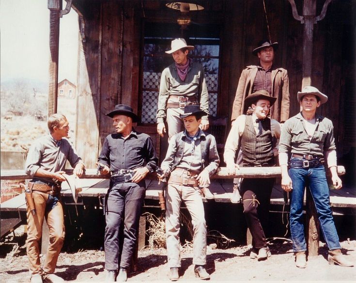 a group of men standing next to each other in front of a wooden structure and building