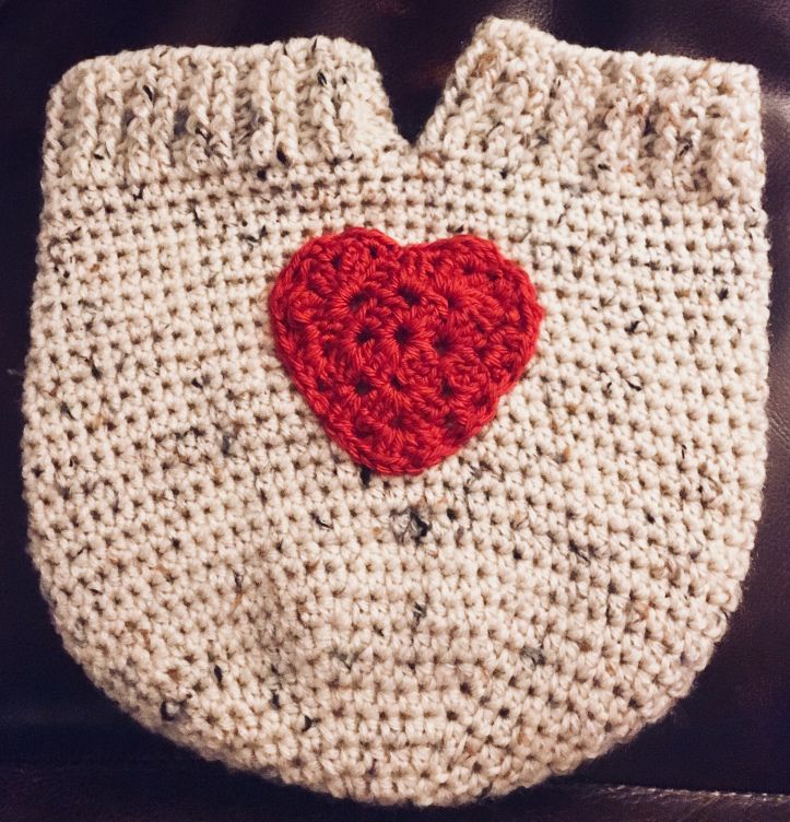 a crocheted bag with a red heart on the front and bottom, sitting on a leather chair