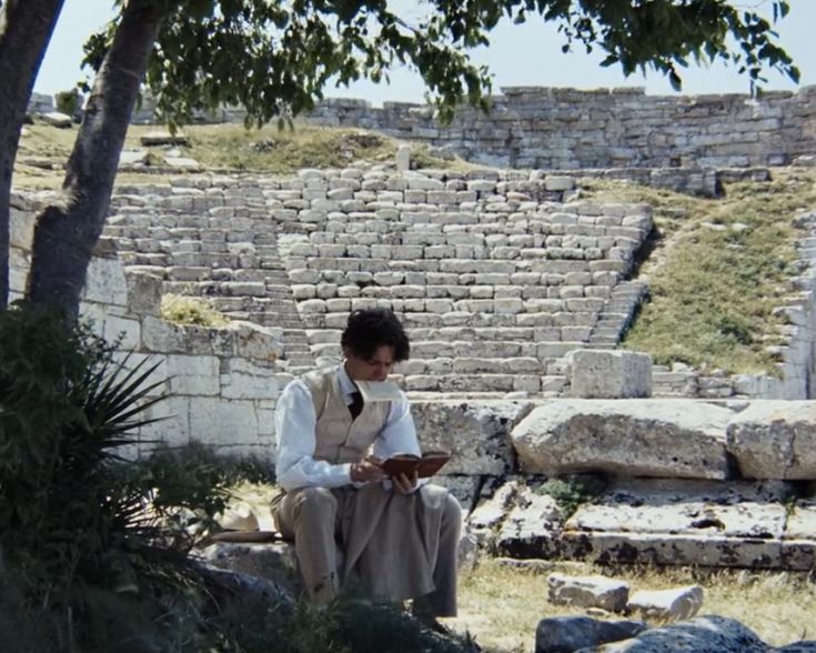 a man sitting on top of a stone bench next to a tree and rock wall