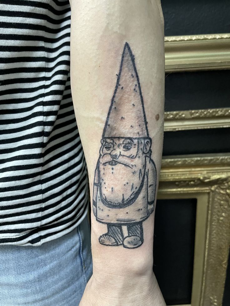 a tattoo on the arm of a person wearing a gnome hat and holding a knife