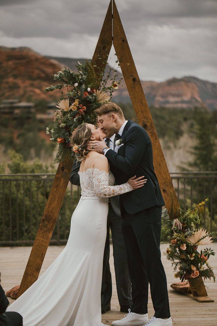 a bride and groom kissing in front of an arch decorated with flowers