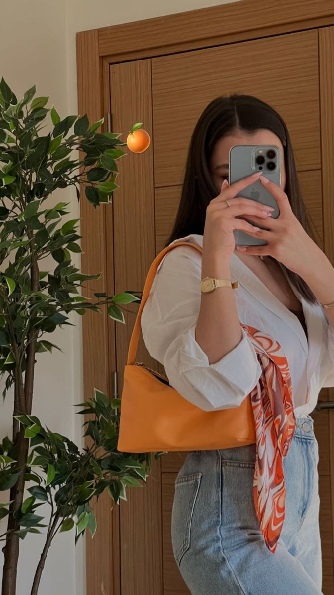 a woman taking a selfie in front of a door with an orange purse on her shoulder