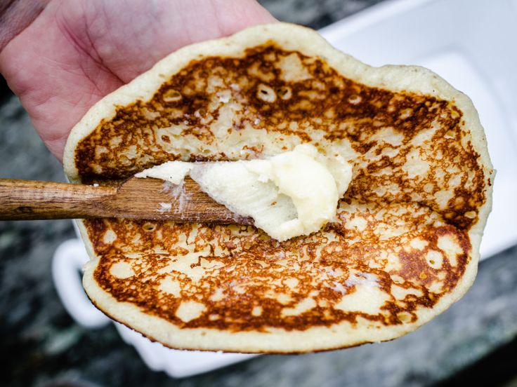 a person is holding a pancake with butter on it and a wooden spoon in their hand