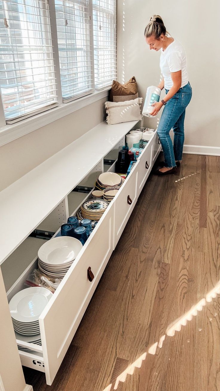 a woman standing next to a white shelf filled with plates and bowls on top of wooden floors