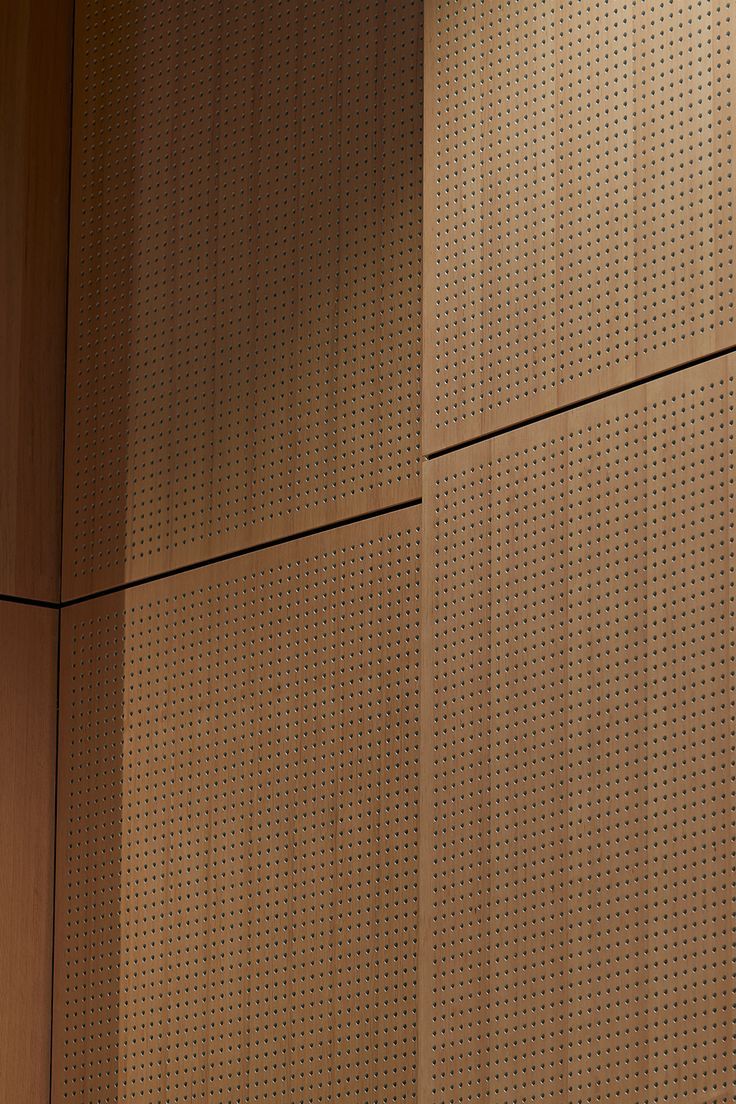 a clock on the side of a building with perforated metal wall behind it