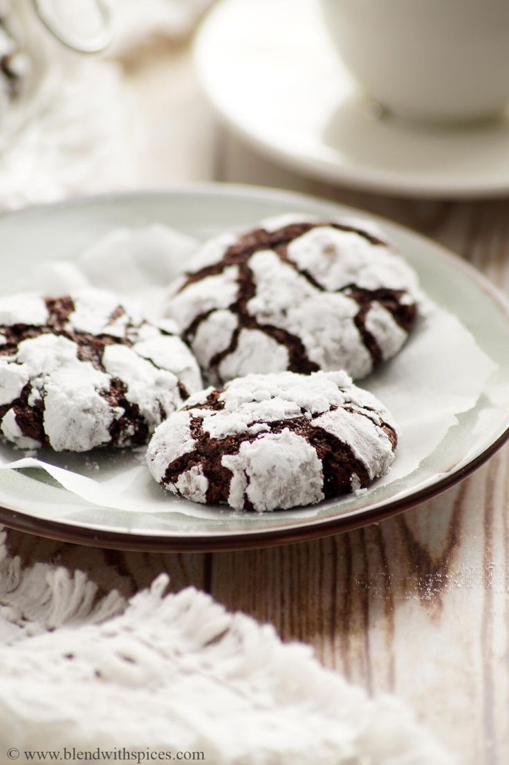 three chocolate crinkle cookies on a white plate next to a cup and saucer