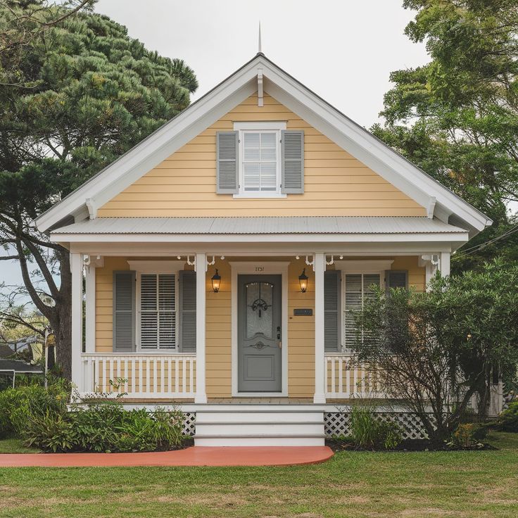 a small yellow house with white trim and shutters on the front door is shown