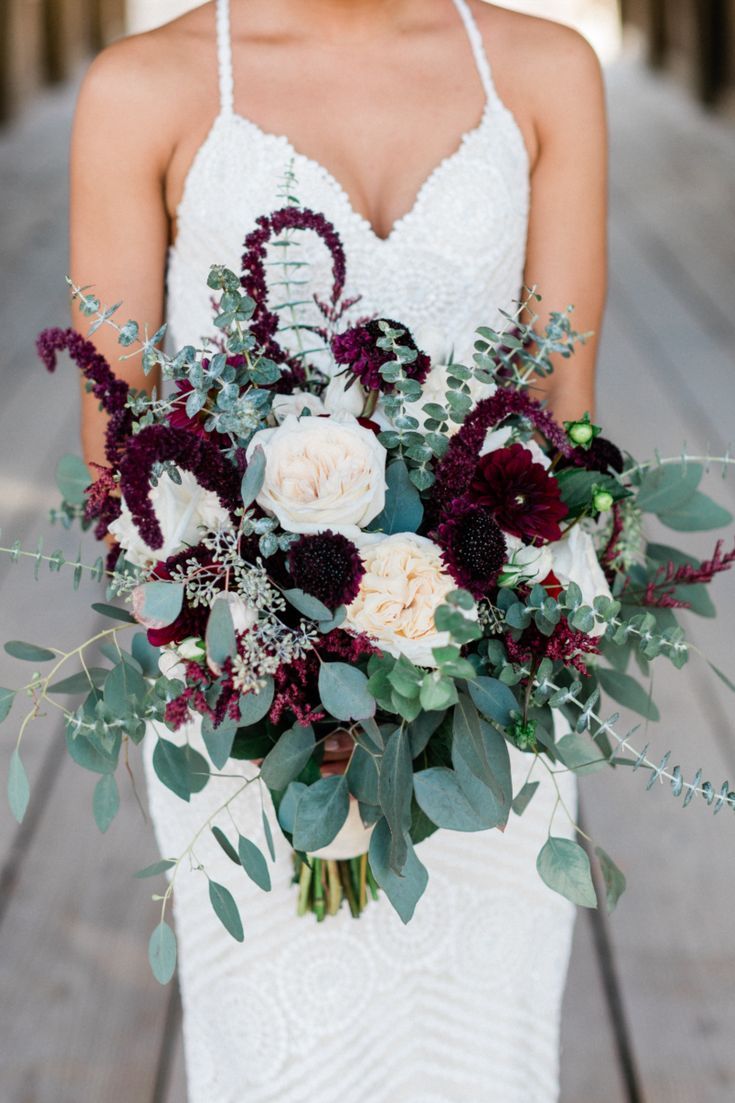 a bride holding a bouquet of flowers and greenery in her hands on the dock