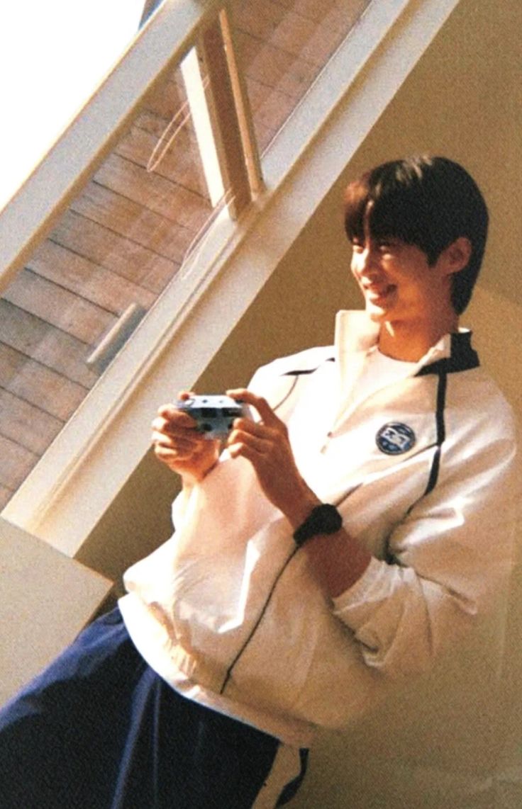 a young man holding a video game controller in his hands while standing next to some stairs