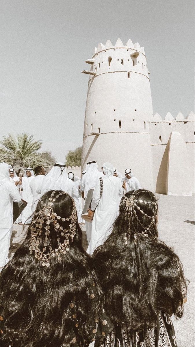 some people are standing in front of a white building and one is wearing long black hair