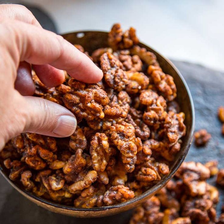 a hand picking up some nuts from a bowl