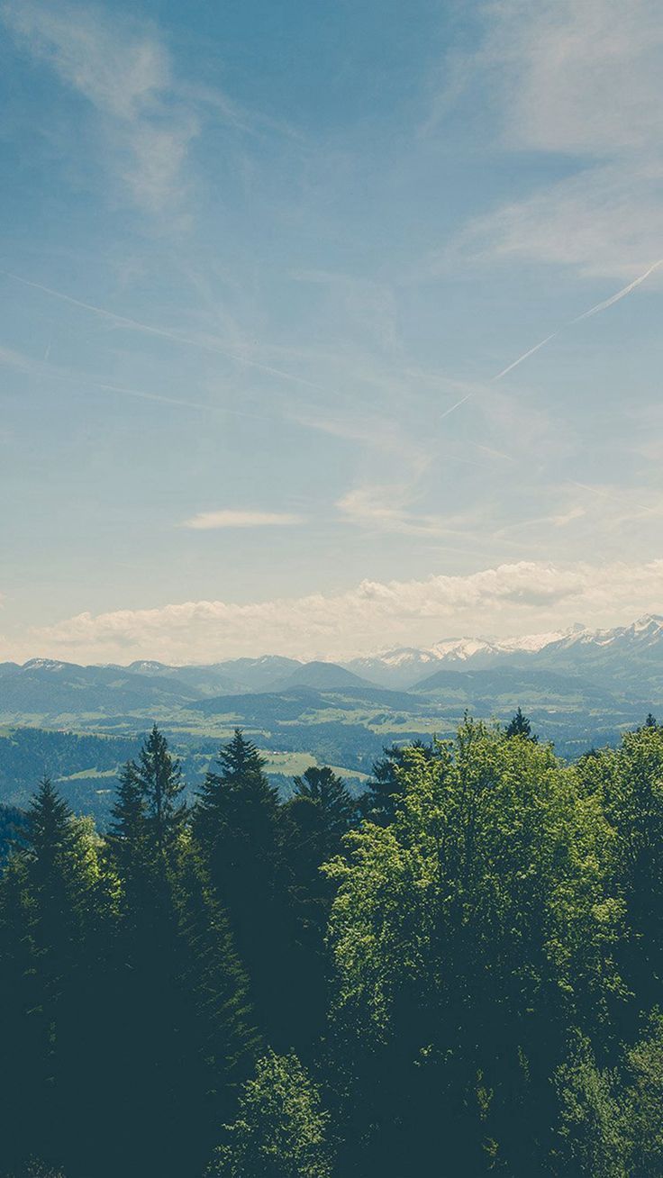 a scenic view of trees and mountains in the distance with a blue sky above them