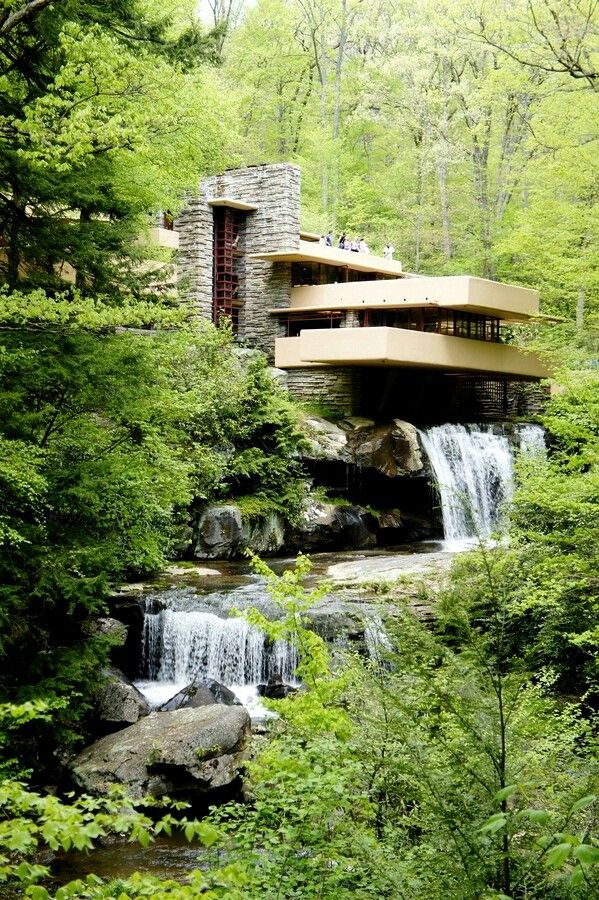 a house in the woods surrounded by trees and rocks with water running down it's side