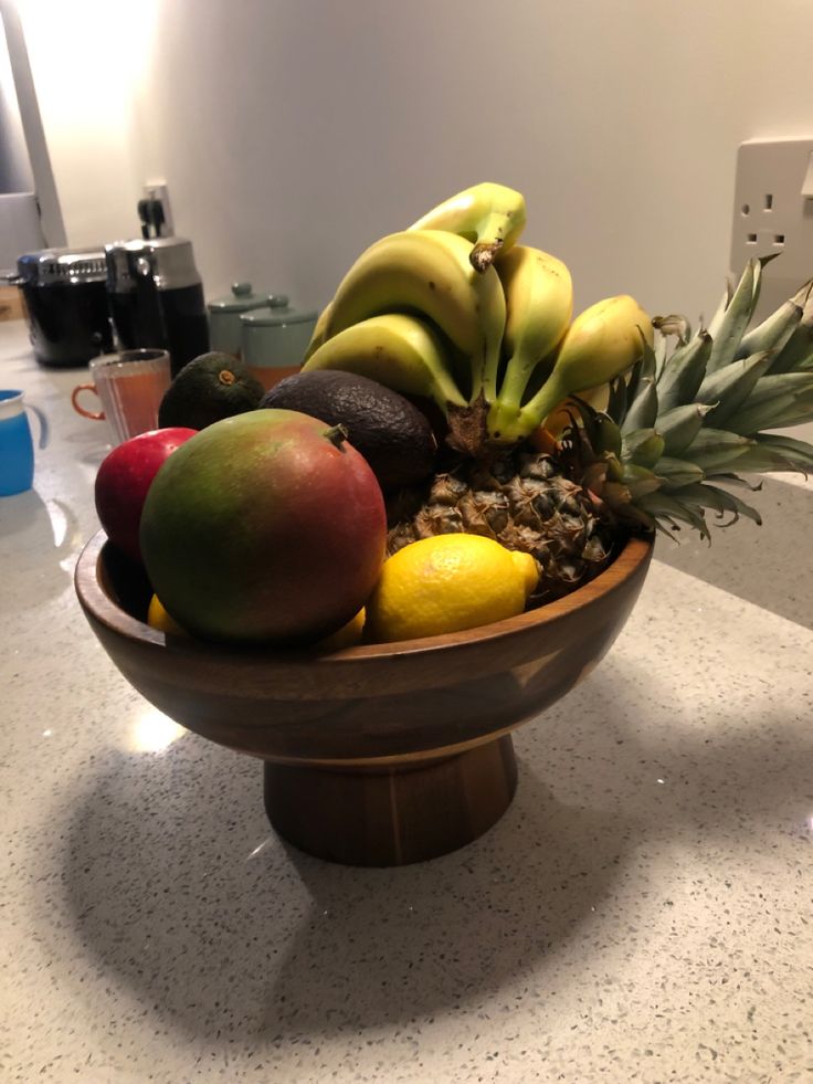 a wooden bowl filled with lots of different types of fruit on top of a counter