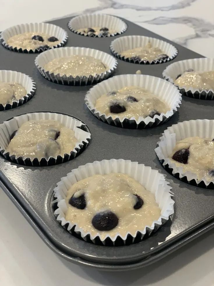 twelve cupcakes with blueberries and white icing sitting on a baking tray