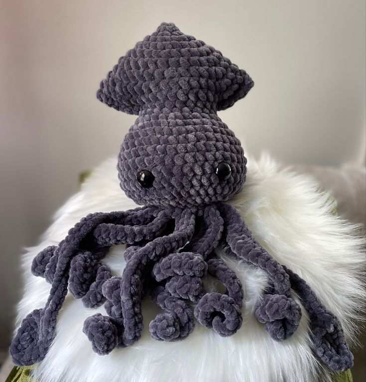 an octopus stuffed animal sitting on top of a white fur covered pillow with black eyes