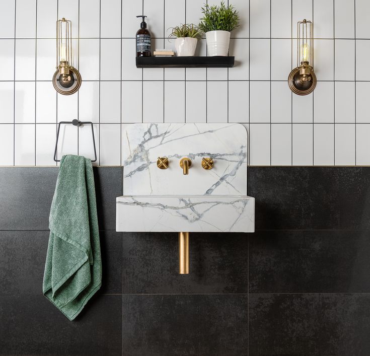 a white sink sitting next to a black counter top in a bathroom with gold faucets