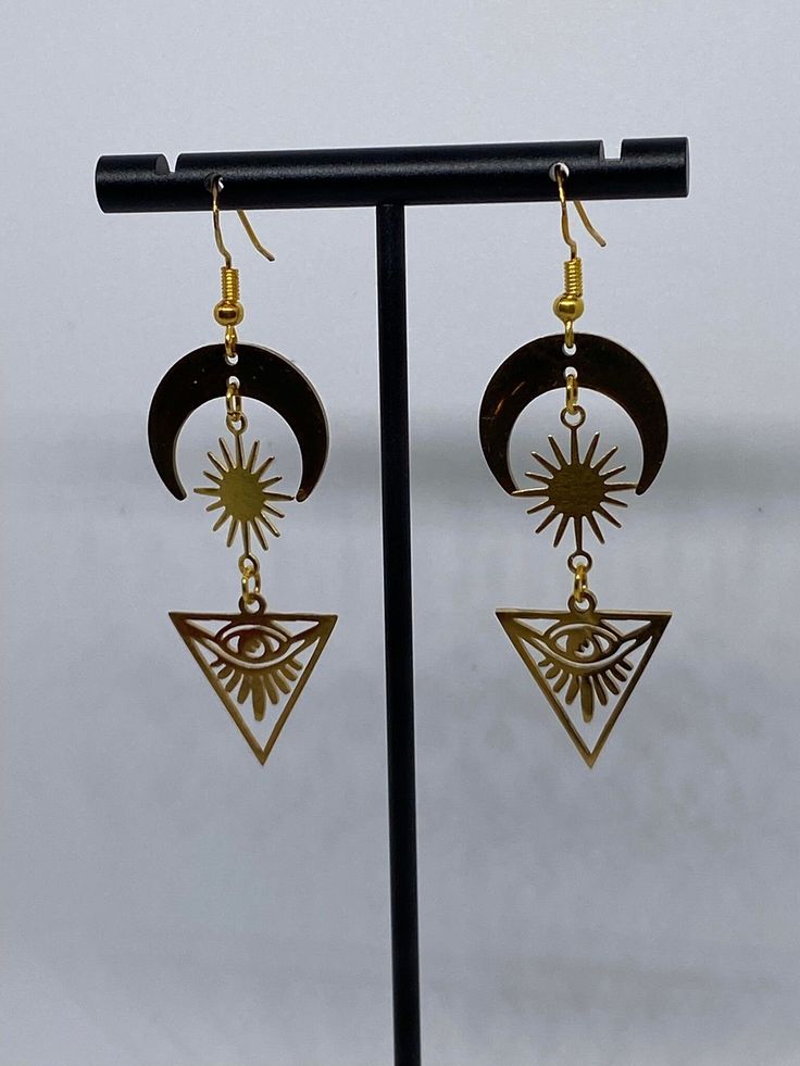 Handmade stainless steel drop earrings featuring a half-moon top, sunburst middle, and celestial/tarot style pyramid bottom Mystical Gold Earrings With Sun And Moon Design, Symbolic Metal Dangle Earrings, Gold Symbolic Earrings With Sun And Moon Design, Symbolic Gold Earrings With Sun And Moon Design, Festival Sun And Moon Dangle Jewelry, Spiritual Sun And Moon Dangle Earrings, Metal Moon Phase Drop Earrings, Moon Phase Metal Drop Earrings, Metal Drop Earrings With Moon Phase