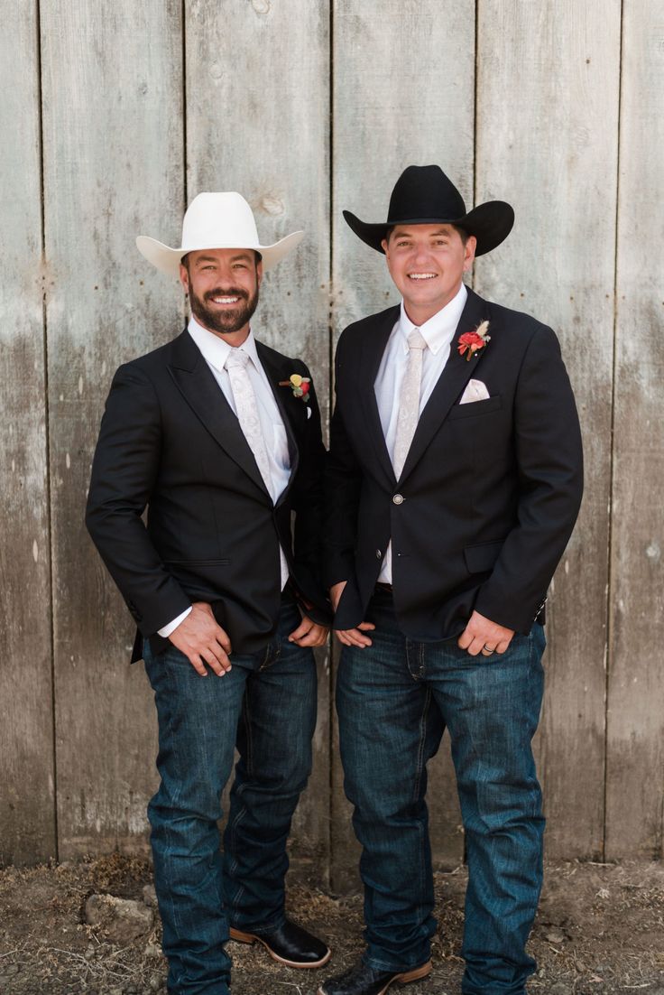 two men standing next to each other in front of a wooden fence wearing cowboy hats