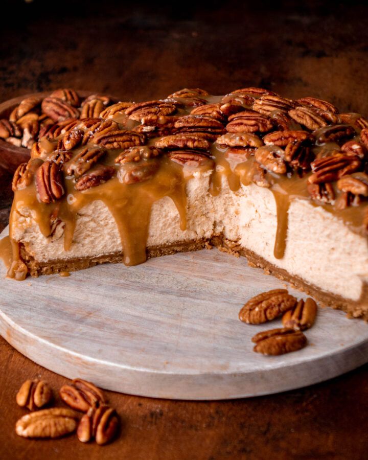 a cheesecake covered in pecans on a cutting board with one slice cut out