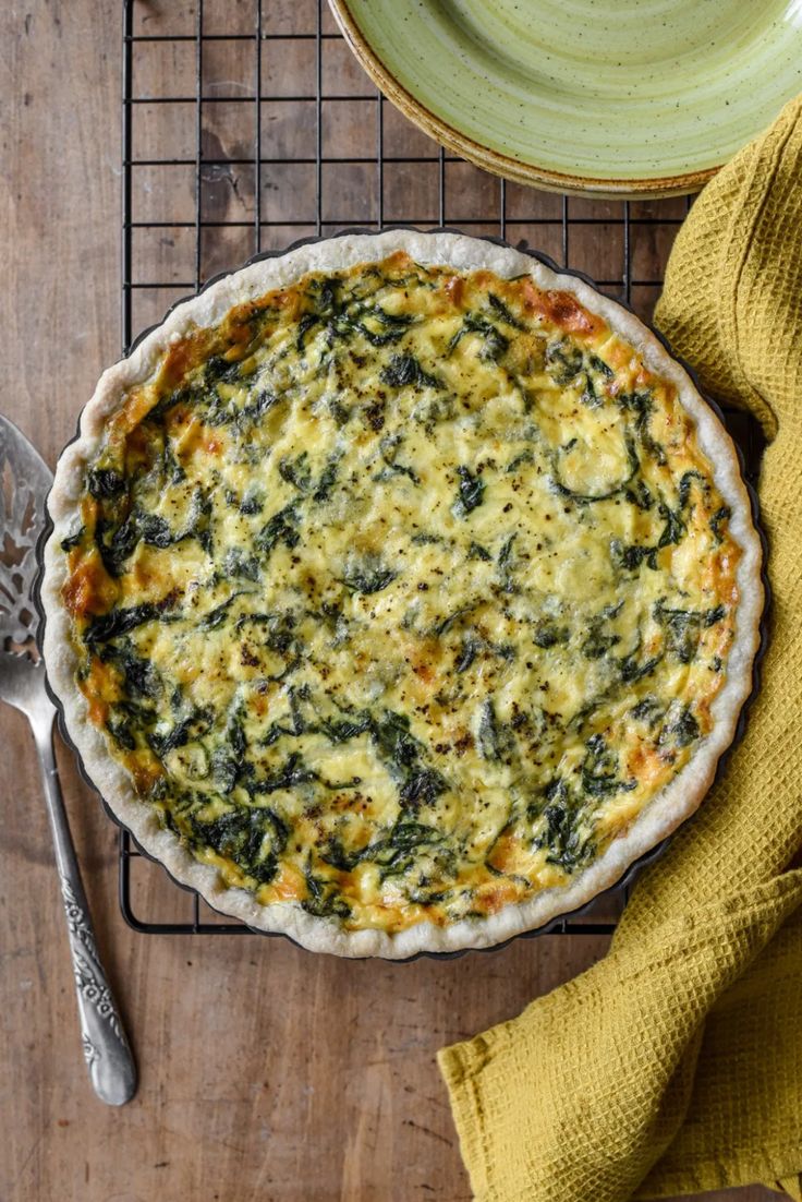 a quiche with spinach and cheese in a pie pan on a wire rack