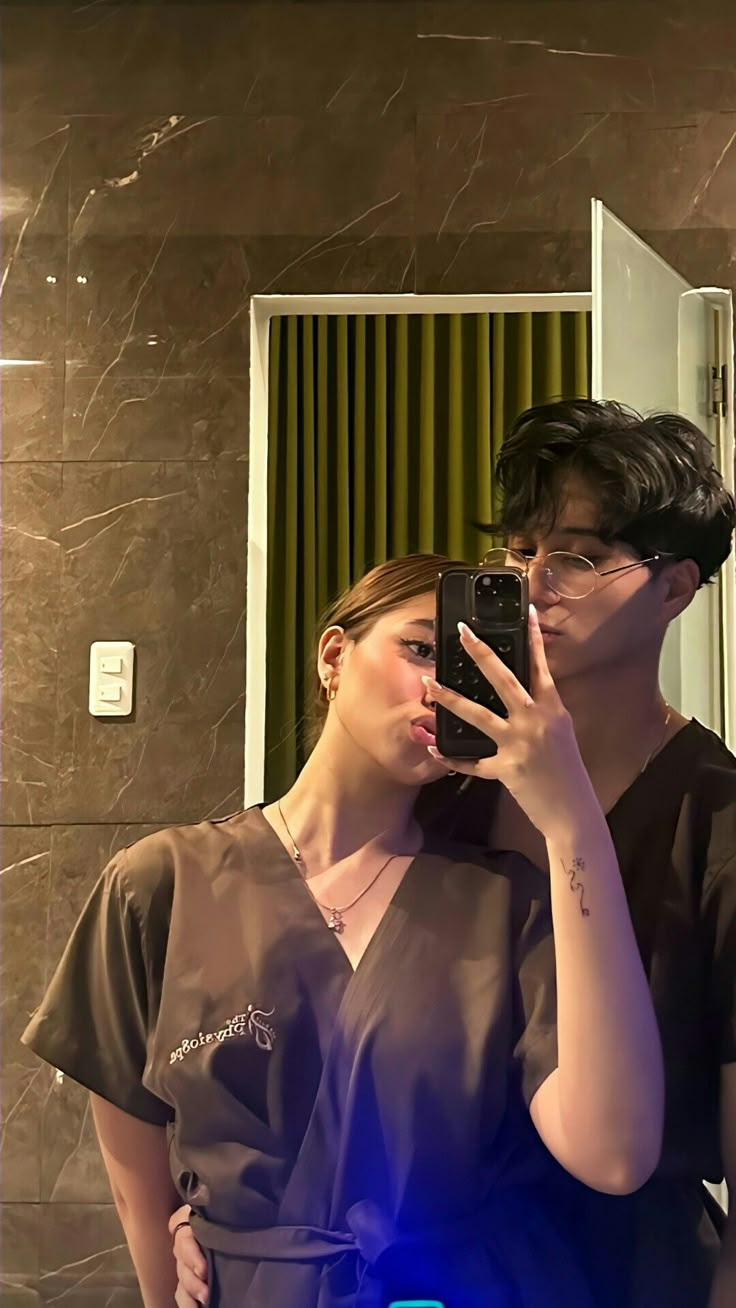 a man and woman standing in front of a mirror taking a selfie with their cell phone