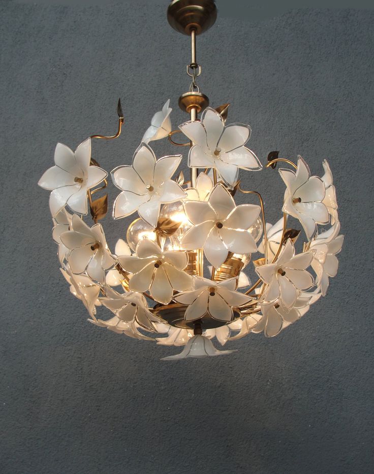 a chandelier with white flowers hanging from it's center point, on a gray wall