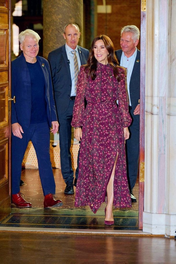 a woman in a purple dress is walking through an open door with two men standing behind her